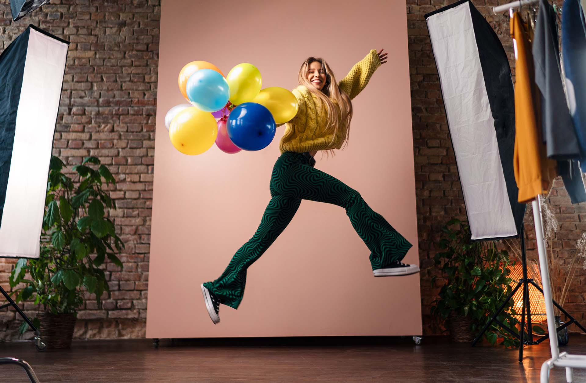 Product Photography Tips: Focus of a photoshoot, lady leaping with balloons wearing a bright yellow jumper, includes backdrop and light boxes.