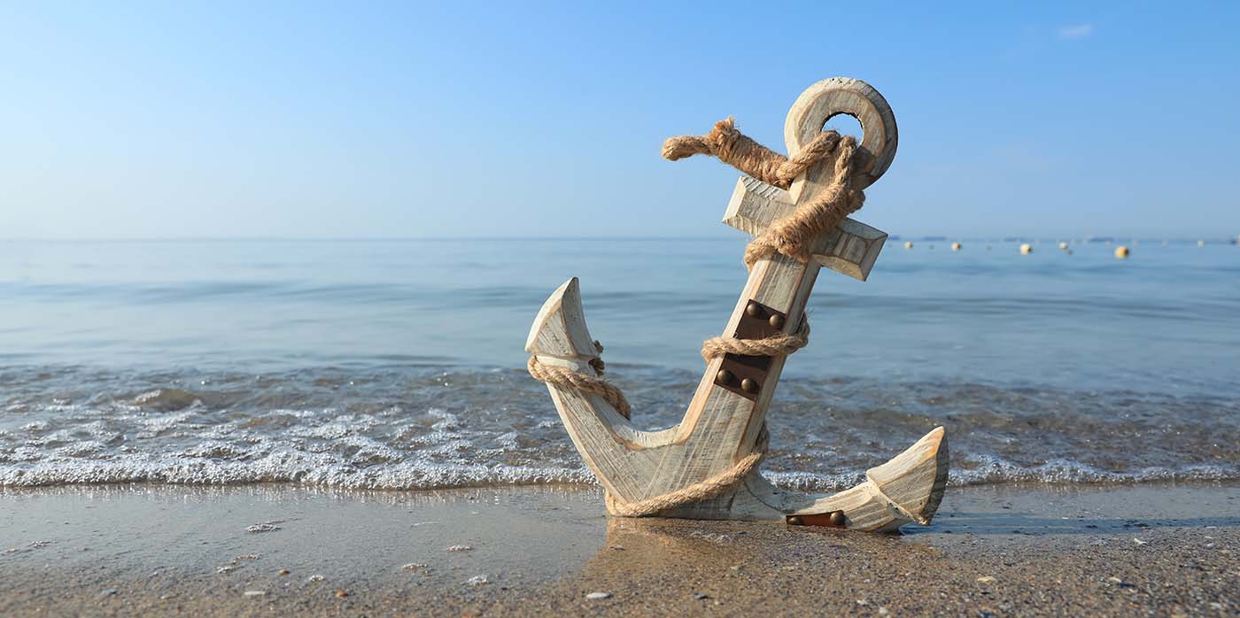 what is anchor test - a picture of a large wooden anchor stood upright on a beach, clear blue sky and sea
