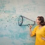 How to Write a Press Release - a lady in a yellow jumper using a drawn megaphone. A small square image used as a thumbnail.