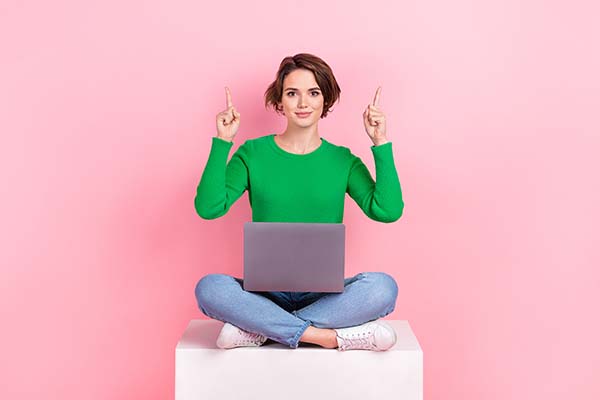 A lady in a green jumper sat crossed legged on a podium with a pink background and a laptop in her lap with her fingers pointing upwards. What should be included on a service page