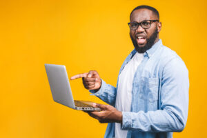 How to Clear Your Browser Cache - this image shows a bright yellow background with a man in glassess pointing at his laptop screen looking frustrated