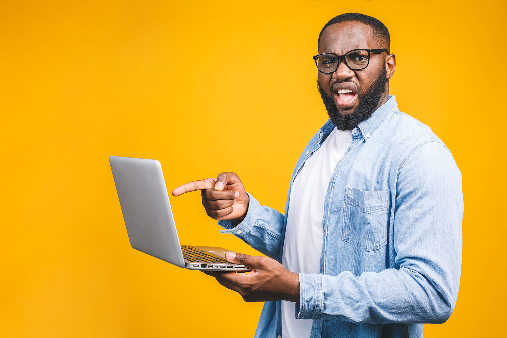 How to Clear Your Browser Cache - this image shows a bright yellow background with a man in glassess pointing at his laptop screen looking frustrated