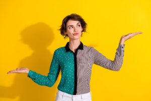 The Difference Between Content That Educates and Content That Converts this image shows a bright yelow background with a lady in a colourful blouse in the foregroud looking thoughtful, she has her arms out to the sides and raised one higher than the other as if balancing or measuring options.